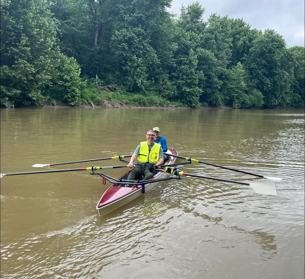 An adaptive athlete smiles as he rows in a two person boat.