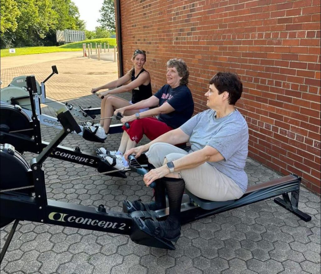 Three women rowing on Concept2 ergometers outdoors at Louisville Adaptive Rowing