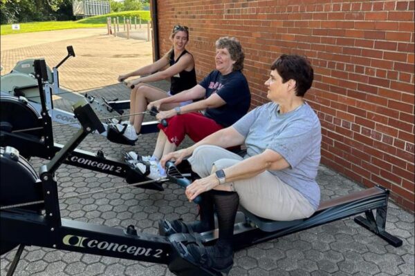 Three women rowing on Concept2 ergometers outdoors at Louisville Adaptive Rowing